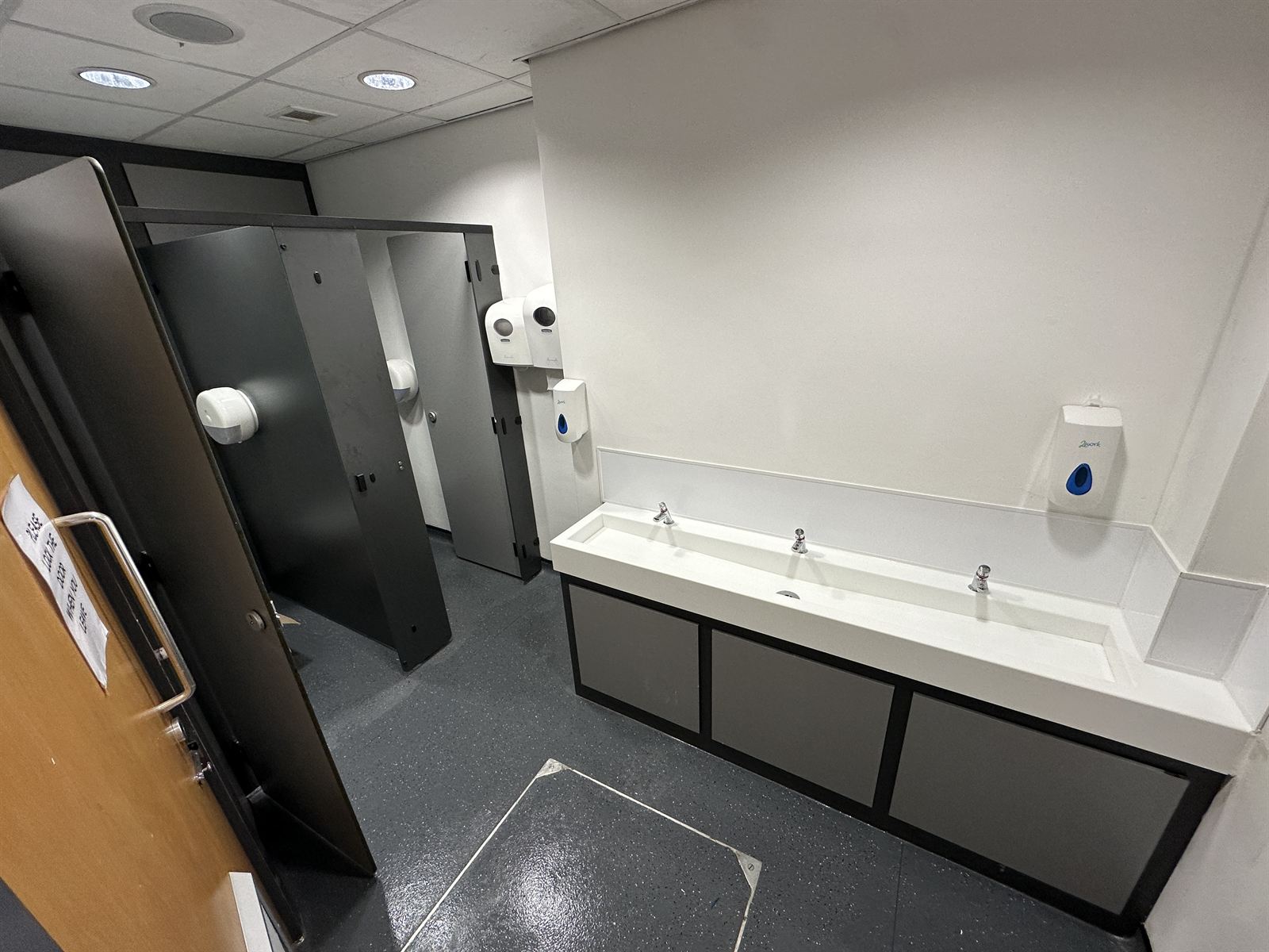 Completed commercial washroom with cubicles and trough sink