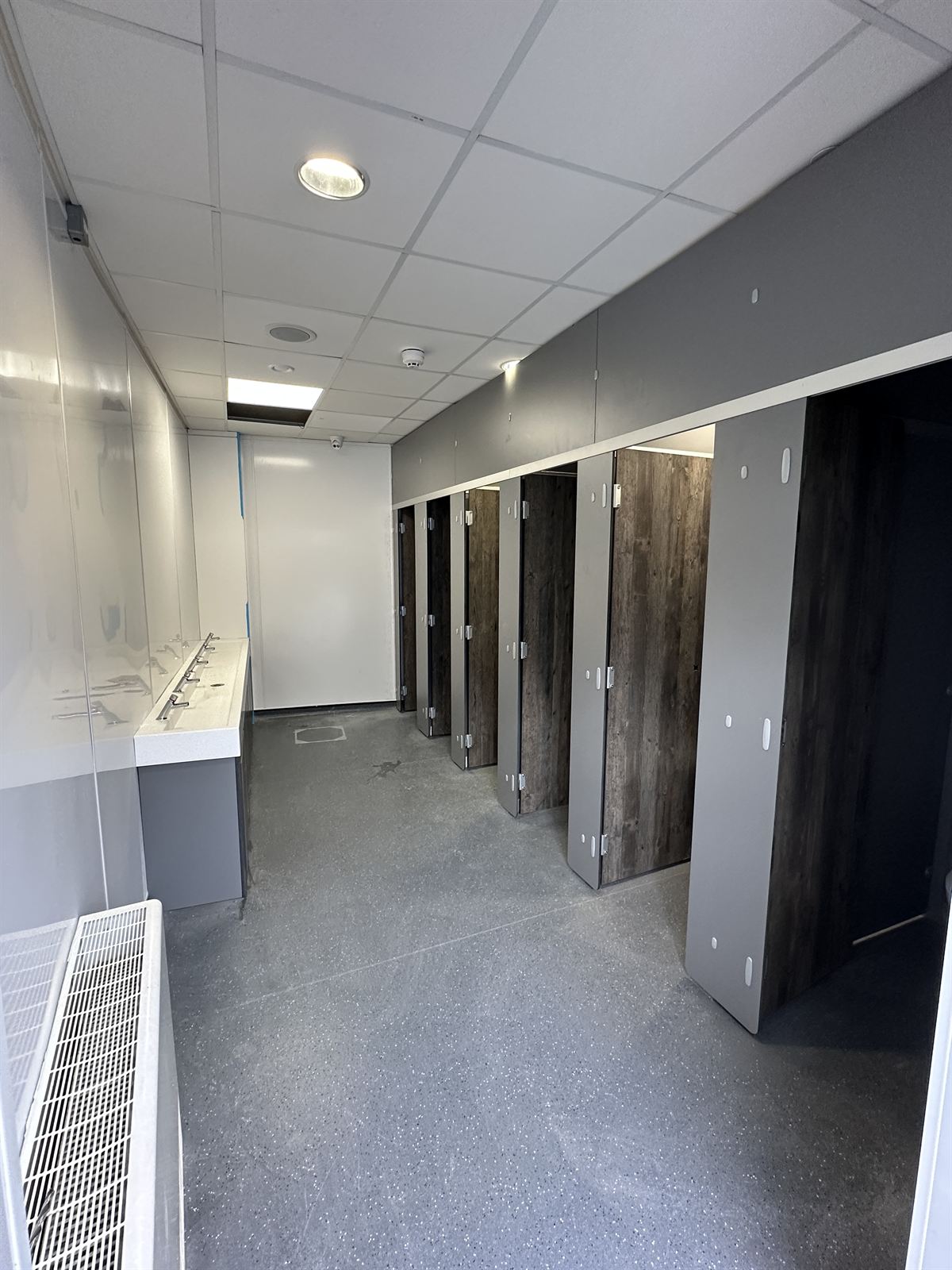 Commercial washroom with wood-effect cubicles and long vanity trough